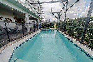 A swimming pool with a glass enclosure, surrounded by a patio area with chairs and a table. - Go!#41 - WINDSOR AT WESTSIDE (Kissimmee)