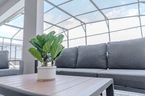 Une plante en pot est posée sur une table en bois dans un espace intérieur moderne, avec un canapé gris et un plafond en verre.
