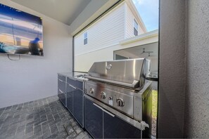 An outdoor kitchen with a stainless steel grill, a built-in sink, and a window overlooking a residential area. - Go!#37 - WINDSOR ISLAND (Davenport)