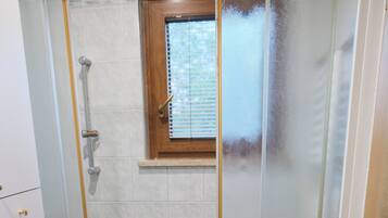 Eine Duschkabine mit Milchglas-Türen, einem kleinen Fenster und einem Handtuch auf dem Boden.