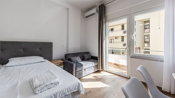 Een hotelkamer met een bed, een bank, een stoel en een balkon met uitzicht op het gebouw.