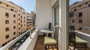 Een balkon met een tafel en twee stoelen, met uitzicht op een woongebied met meerdere gebouwen.