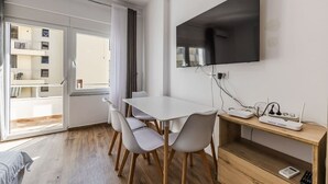 Een moderne kamer met een eettafel, stoelen, een flatscreen televisie aan de muur en een houten bureau met een router.