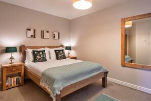 A bedroom with a wooden bed, two bedside tables with lamps, a mirror, and a bookshelf. - Cozy House Near Whitby Harbour (Bude)