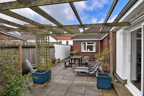 A covered patio area with a wooden pergola, a table with chairs, and potted plants. - Cozy House Near Whitby Harbour (Bude)