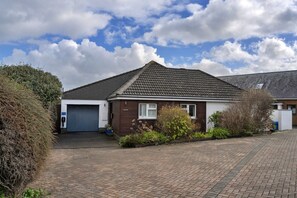 A residential house with a garage, a brick driveway, and a garden area with various plants. - Cozy House Near Whitby Harbour (Bude)