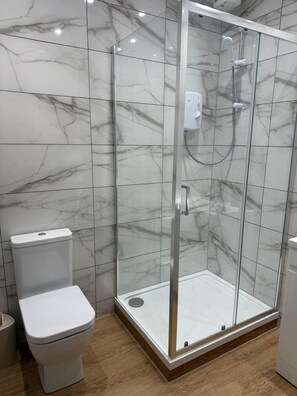 A bathroom with a glass-enclosed shower, a toilet, and marble-patterned walls. - Bright 3BR • Rose Street • Heart of Edinburgh (Edinburgh)