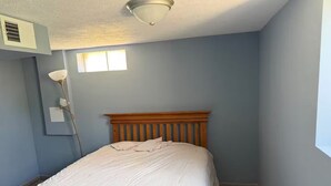 Ein Schlafzimmer mit einem hölzernen Bett, einer Deckenleuchte, einem Fenster und einem Wandlüfter.