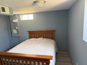 Ein Schlafzimmer mit einem hölzernen Bett, einer Deckenleuchte, einem Fenster und einem Wandlüfter.