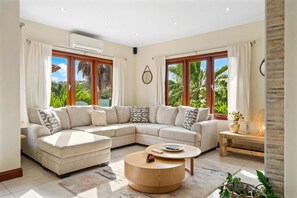 A modern living room with a sectional sofa, a round coffee table, and large windows with curtains. - 5BR Villa w/ Private Pool & Palapa, Noord Aruba (Noord)