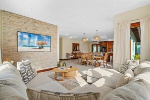 Ein modernes Wohnzimmer mit großem Flachbildfernseher, einem Essbereich und einer Küche im Hintergrund.