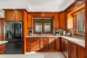 Eine moderne Küche mit Holzschränken, einem Edelstahlkühlschrank und einem Fenster mit Jalousien.