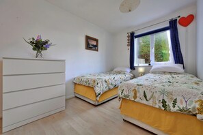 A bedroom with two beds, a dresser, a window with curtains, a wall-mounted picture, and a heart decoration. - Bungalow in Seaside Town of Pwllheli (Pwllheli)