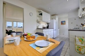 A modern kitchen with white cabinets, a dining table set with plates, cups, and a croissant, and a view of the outside through a window. - Bungalow in Seaside Town of Pwllheli (Pwllheli)