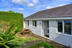 A single-story house with a white exterior, a tiled roof, and a small patio area with a table and chairs. - Bungalow in Seaside Town of Pwllheli (Pwllheli)