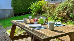 Ein Holztisch für ein Picknick draußen, mit Tellern, Tassen, einer Kanne und einem Einmachglas Marmelade.