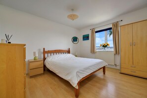 A bedroom with a wooden bed, a nightstand, a wardrobe, and a window with a view. - Bungalow in Seaside Town of Pwllheli (Pwllheli)