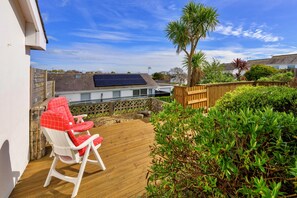 A deck with a red and white chair, a wooden fence, and a solar panel on a house roof. - Bungalow in Seaside Town of Pwllheli (Pwllheli)