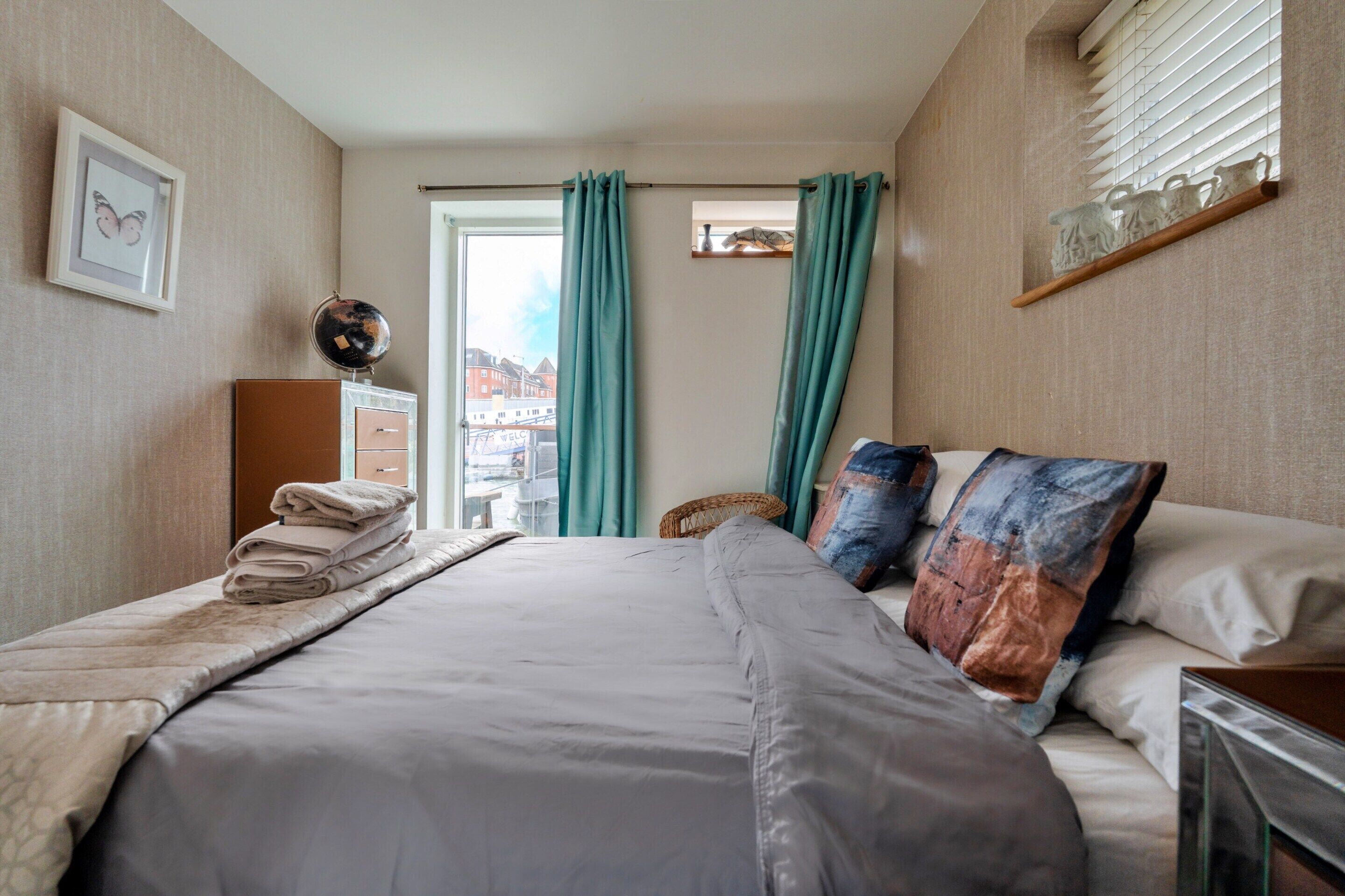 A hotel room with a bed, a bedside table, a lamp, a framed picture, and a view of the outside.
