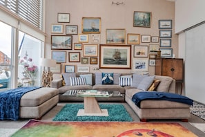 A living room with a sofa set, a coffee table, and a wall adorned with framed maritime paintings.
