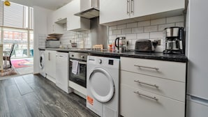 Una cocina moderna con armarios blancos, horno empotrado, lavadora y cafetera.