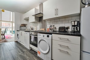 A modern kitchen with white cabinets, a built-in oven, a washing machine, and a coffee maker.