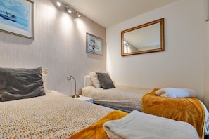 A hotel room with two beds, a bedside table, a lamp, and a mirror.