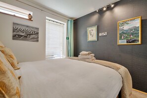 A bedroom with a bed, a window with blinds, a wall with framed pictures, and a wall-mounted light fixture. - Houseboat in Central Liverpool (Liverpool)