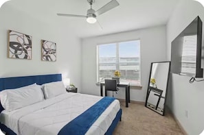 Un dormitorio con cama, escritorio, silla, ventilador de techo y obras de arte en la pared.