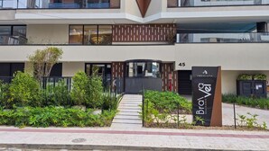 Un edificio moderno con un logotipo destacado, un acceso con portones y un cartel que indica que es un complejo residencial.