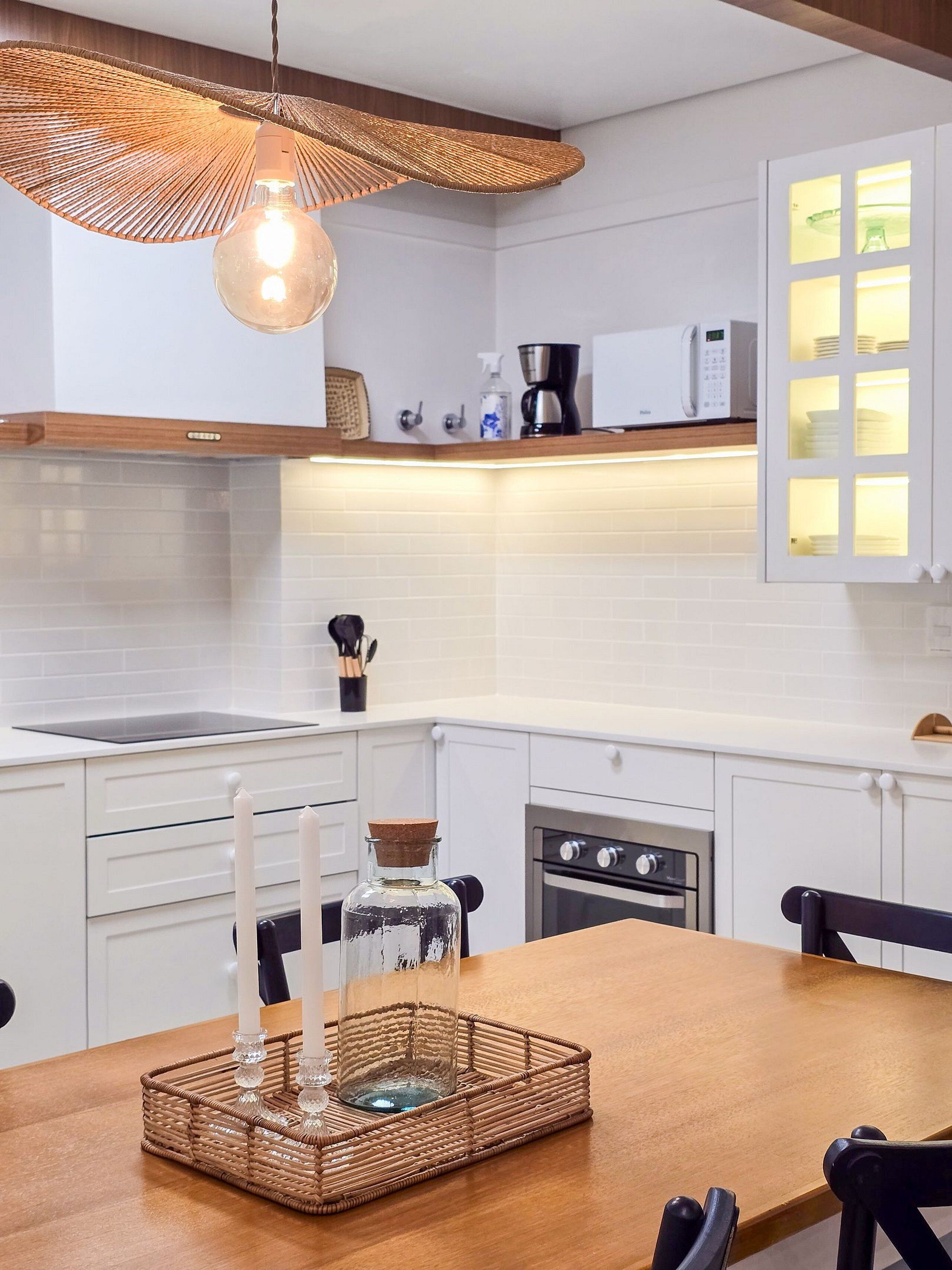 A modern kitchen with white cabinetry, a wooden dining table, and a hanging light fixture.