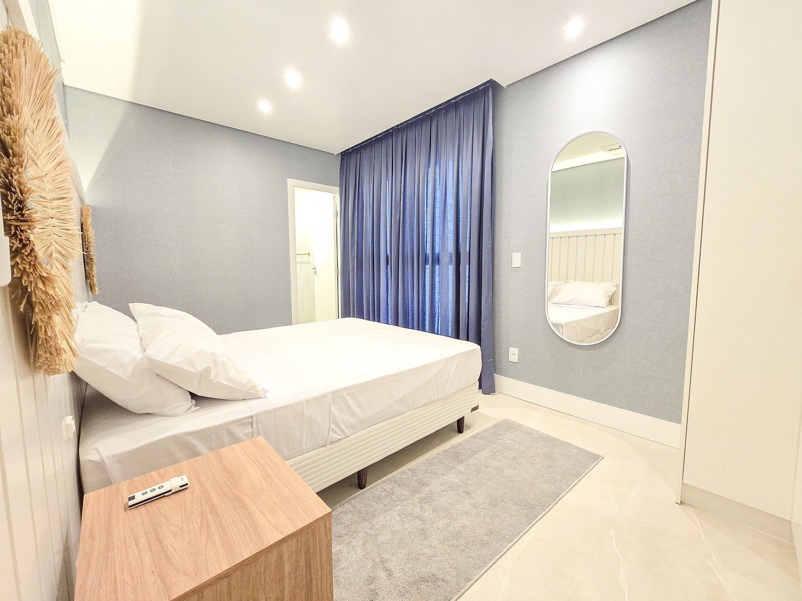 Ein modernes Schlafzimmer mit Bett, Nachttisch, Spiegel und Blick ins Badezimmer.