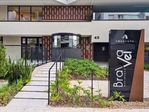 A modern building entrance with a glass facade, a sign for 'Brava Residence,' and a number '45' indicating the address.