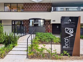 Entrada de um edifício moderno com fachada de vidro, uma placa com 'Brava Residence' e o número '45' indicando o endereço.
