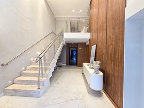 A modern interior with a marble staircase, a wooden accent wall, and a reception desk. - Bravavel na Praia Brava by LikeHome (Balneário Camboriú)