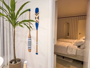 A bedroom with a bed, a potted plant, and two wooden paddles on the wall. - Bravavel na Praia Brava by LikeHome (Balneário Camboriú)