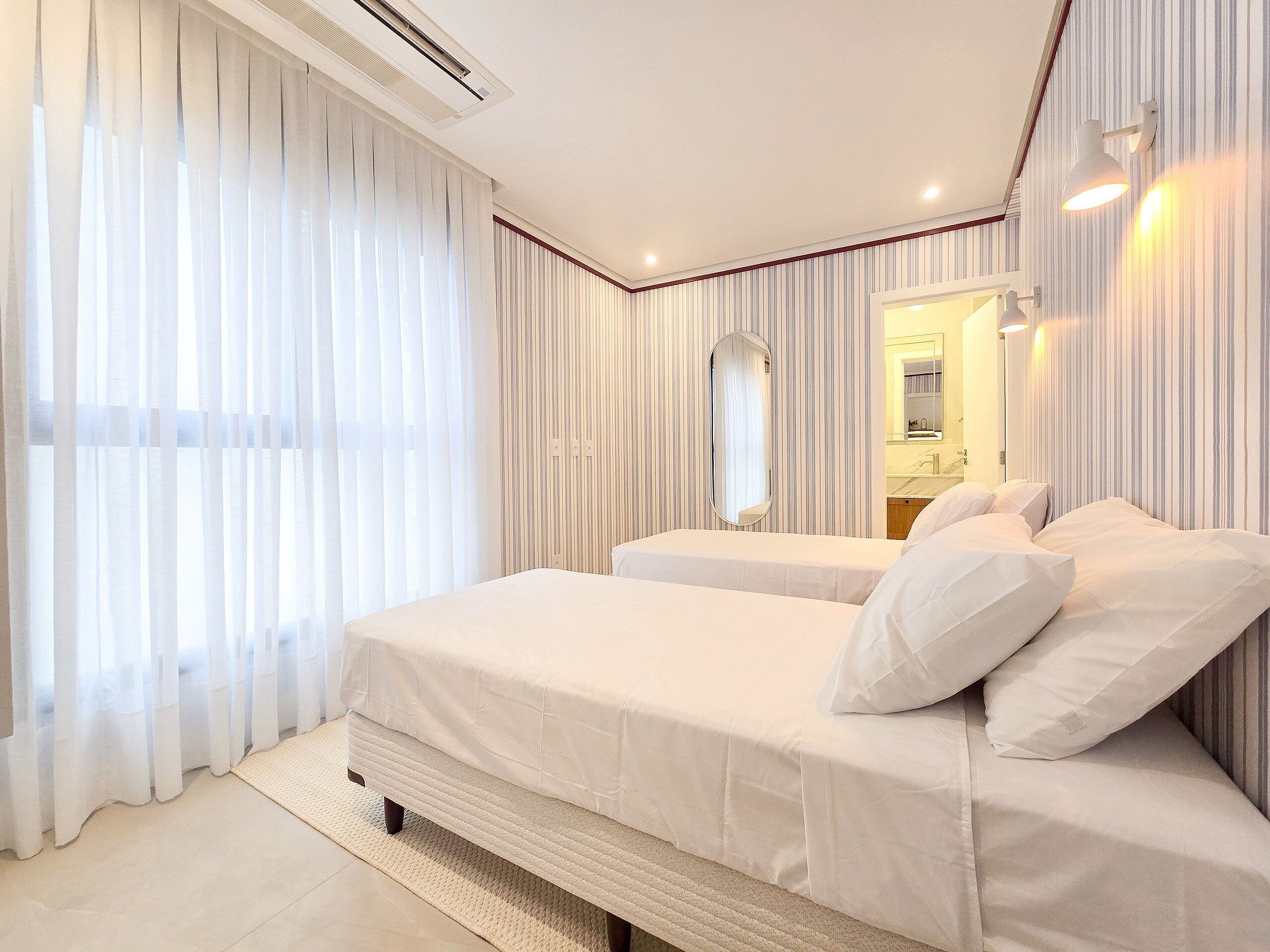 Quarto de hotel com uma cama grande, um espelho e uma janela com cortinas.