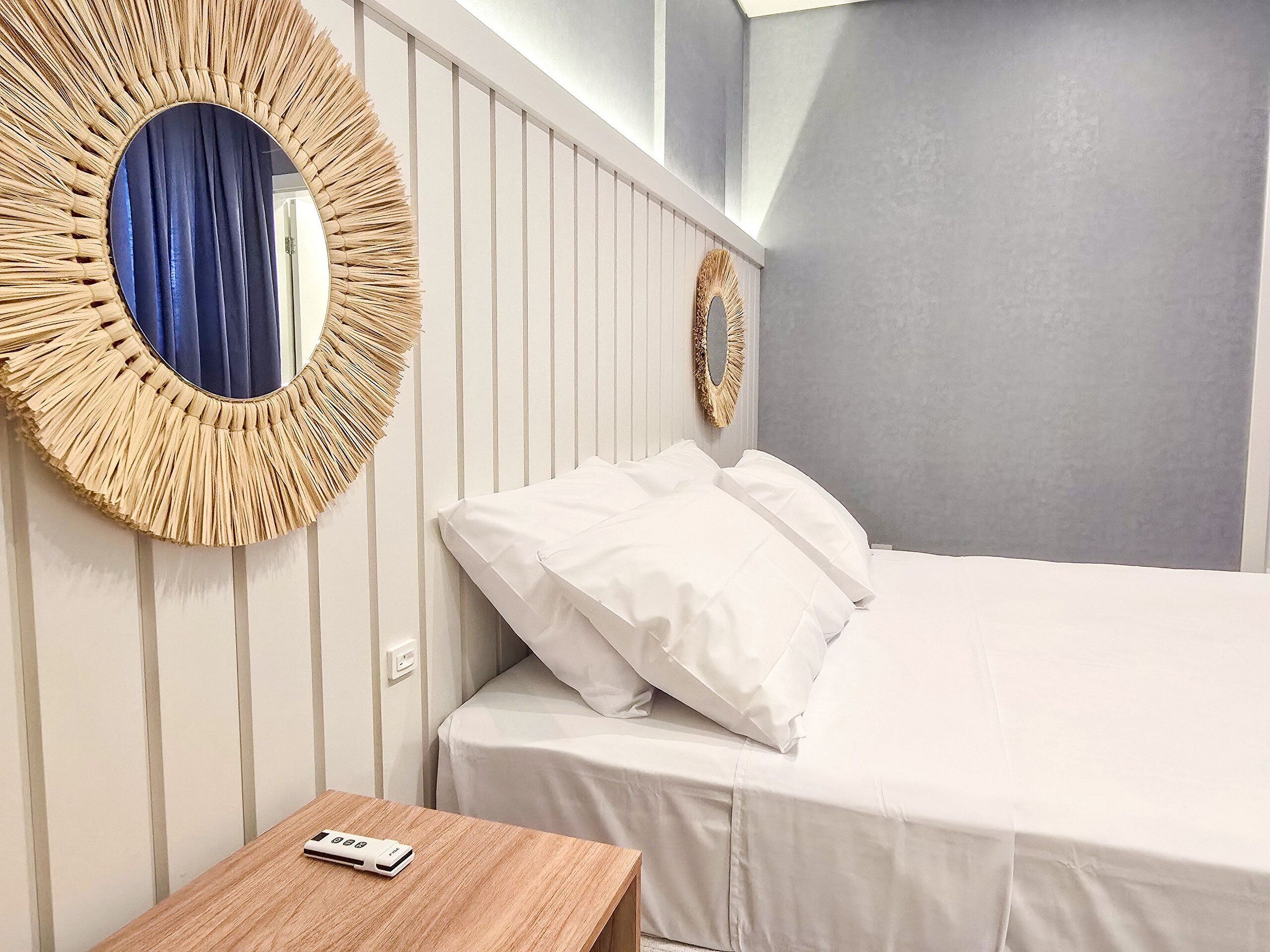 A hotel room with a bed, a bedside table, and two wall-mounted mirrors.