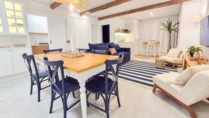 Una sala de estar moderna con comedor, que incluye una mesa de comedor de madera, sillas oscuras, un sofá azul y un sillón blanco.