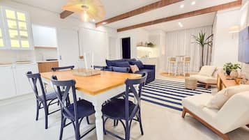 Uma sala de estar moderna com área de jantar, destacando uma mesa de jantar de madeira, cadeiras escuras, um sofá azul e uma poltrona branca.