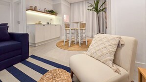 Ett modernt vardagsrum med en soffa, en fåtölj, en köksdel och ett matbord.