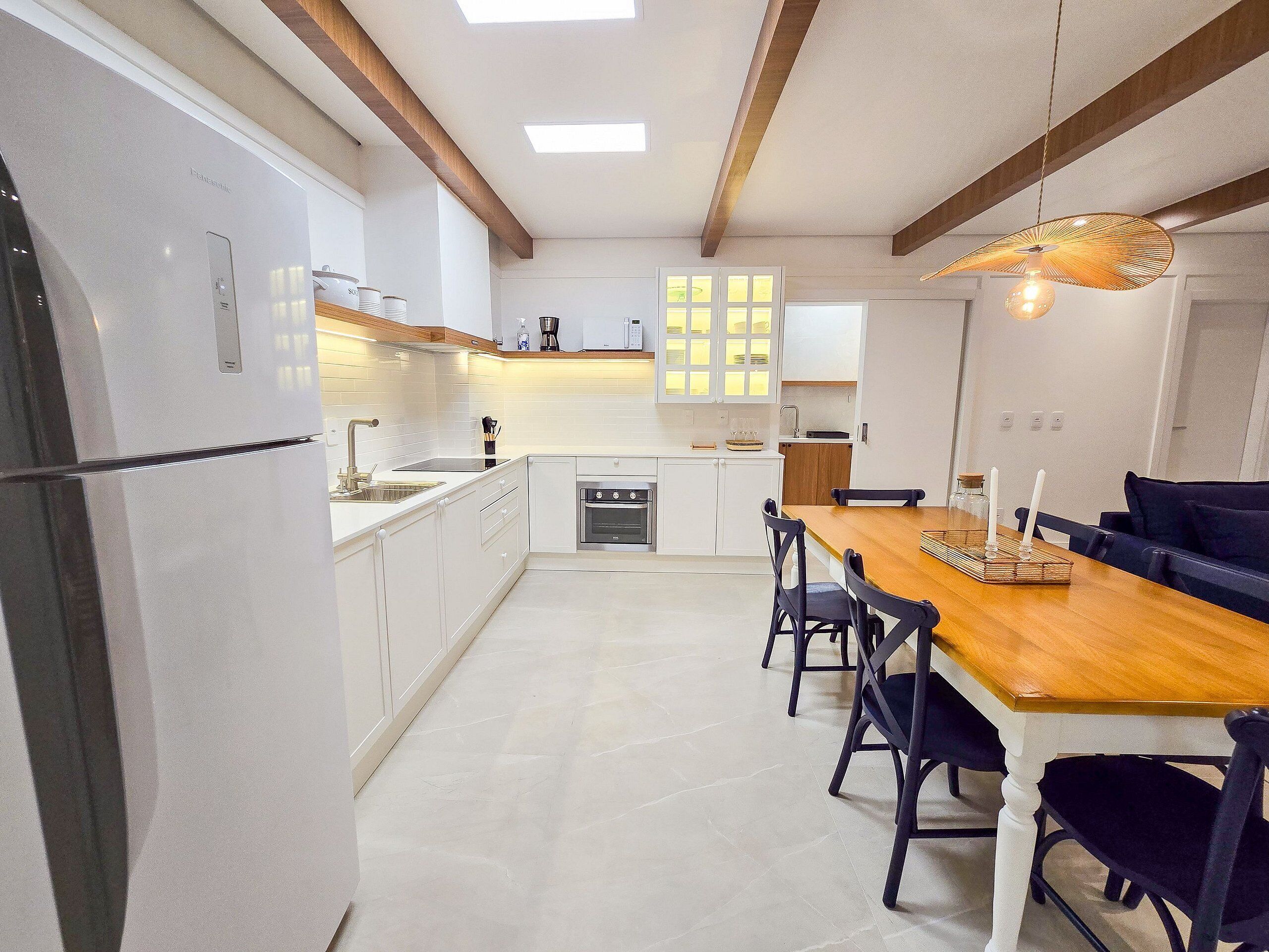 A modern kitchen with white cabinetry, a wooden dining table, and black chairs.