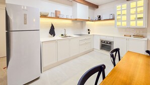 Una cocina moderna con armarios blancos, horno empotrado y comedor con mesa y sillas de madera.