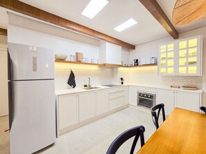 A modern kitchen with white cabinetry, a built-in oven, and a dining area with a wooden table and chairs.