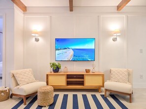 A living room with a television on the wall, two chairs, a wooden console table, and a striped rug. - Bravavel na Praia Brava by LikeHome (Balneário Camboriú)