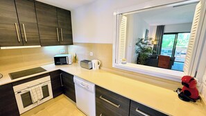 A modern kitchen with dark wood cabinets, a microwave, toaster, and a dishwasher. - Luxury apartment with pool views from a large terrace on world class golf resort (MC)