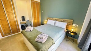 A hotel room with a bed, a desk, a chair, and a nightstand with a lamp.