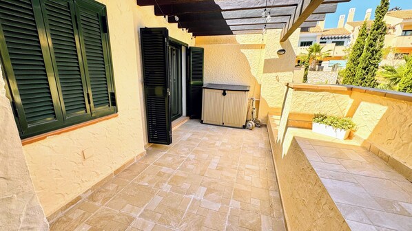A covered outdoor area with a tiled floor, a wooden bench, and a small garden bed with plants.