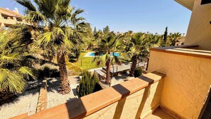 A balcony with a view of a pool and palm trees. - Luxury apartment with pool views from a large terrace on world class golf resort (MC)