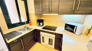 A compact kitchen with a sink, stove, microwave, and a coffee maker.